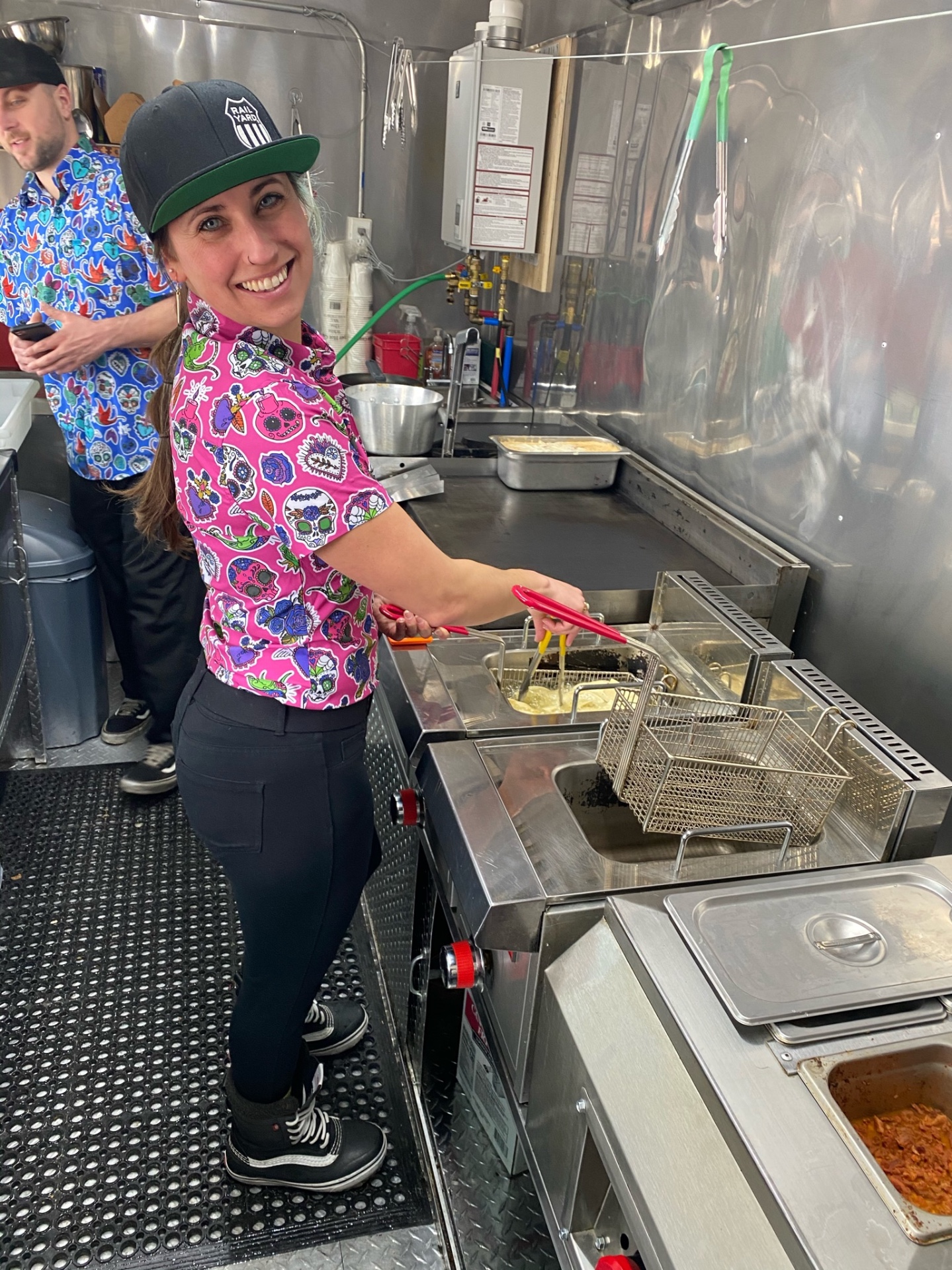 A cook in a sugar-skull shirt working the fryers inside the food truck