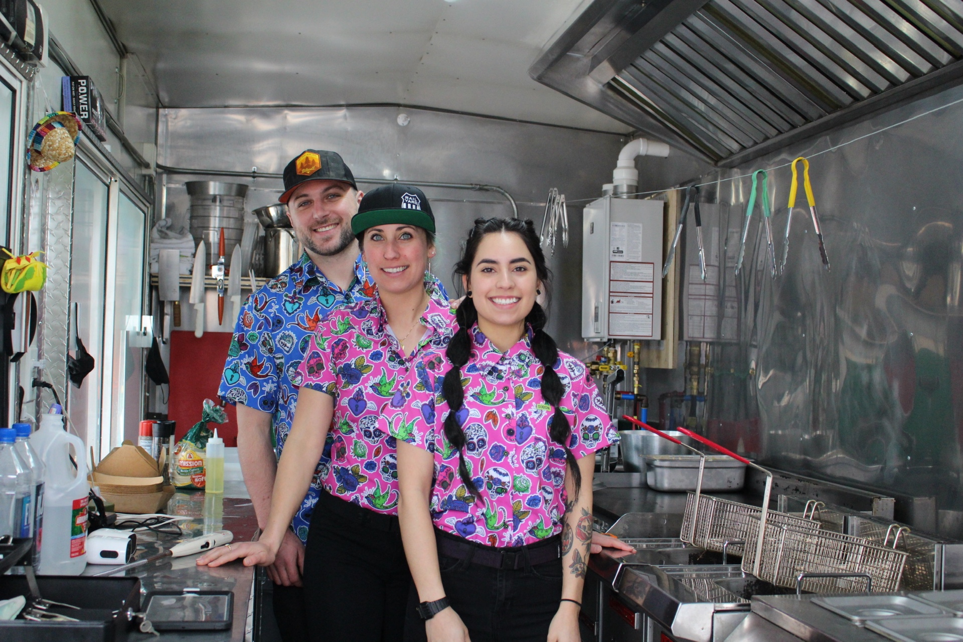 Three Shreddy's crew members in sugar-skull shirts inside the food truck